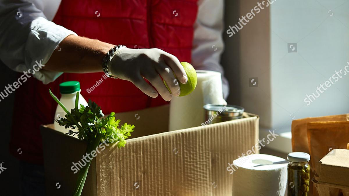 A gloved hand filling a box with healthy foods