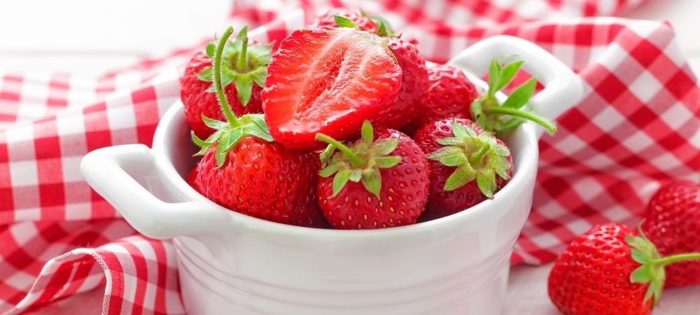 strawberries in a white bowl with a checkered tablecloth