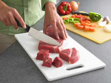 person cutting meat on a separate cutting board from fresh produce 