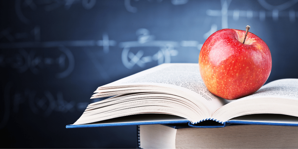 apple on a book in a classroom with a blackboard in the background