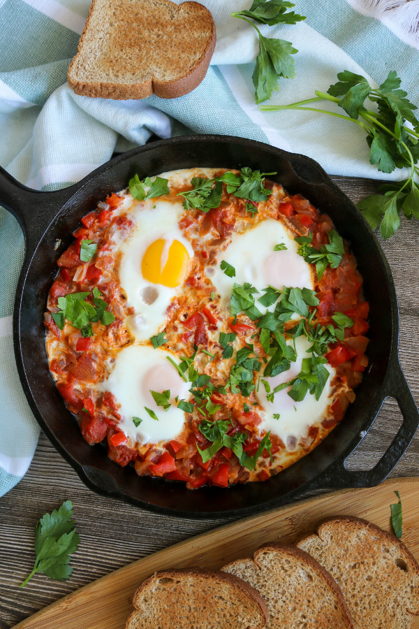 Shakshuka in a skillet with whole wheat bread slices and parsley