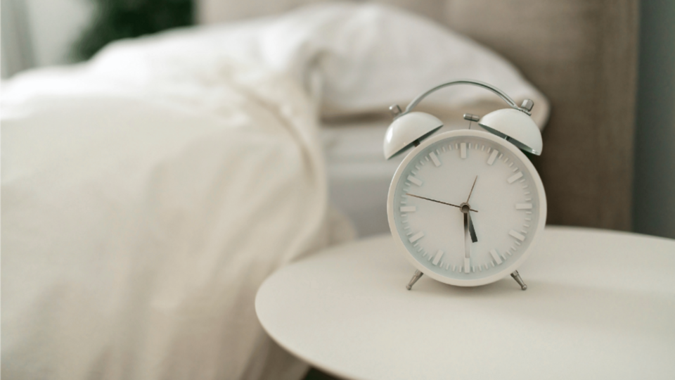 alarm clock on a table next to a bed