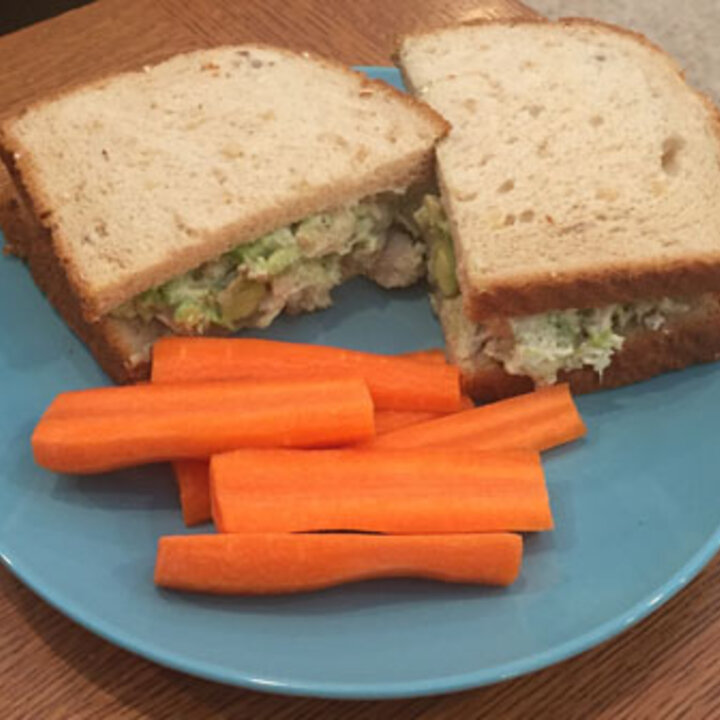 Chicken avocado sandwich on a plate with carrot sticks