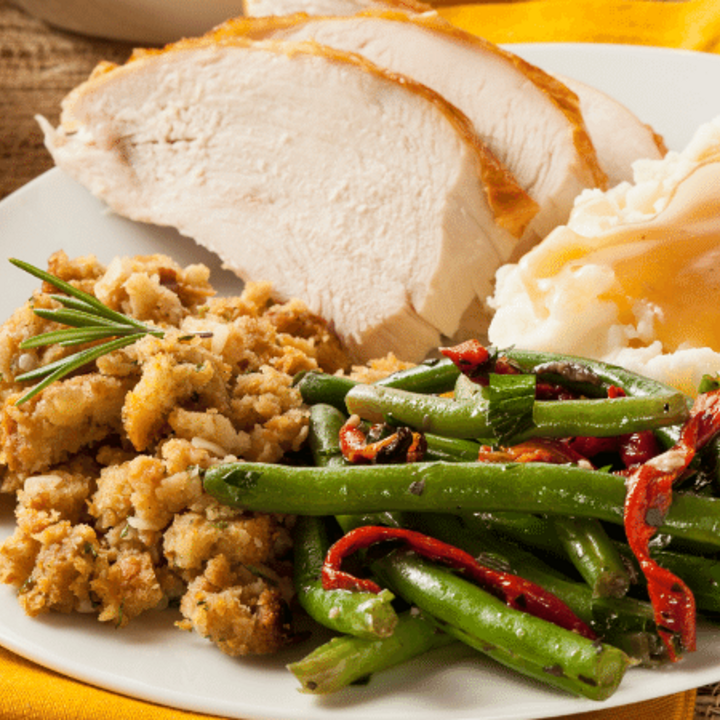 A Thanksgiving dinner plate with turkey, stuffing, mashed potatoes and gravy, and green beans.