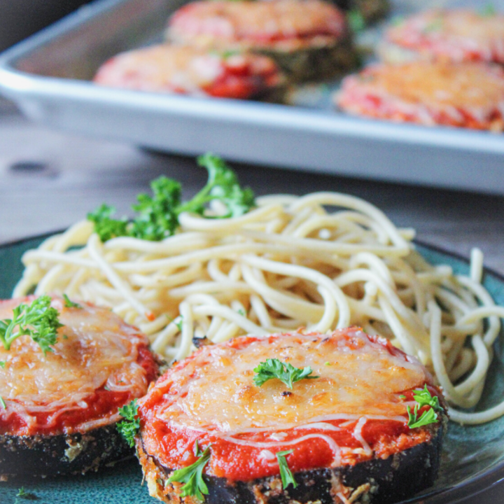 Baked Eggplant parmesan on a plate with whole wheat spaghetti and parsley