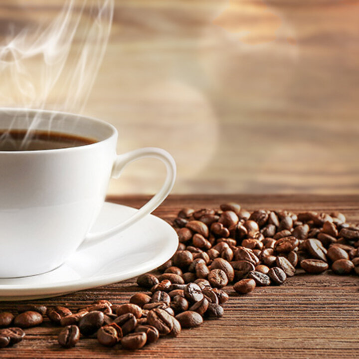 Hot cup of coffee on a saucer surrounded by coffee beans