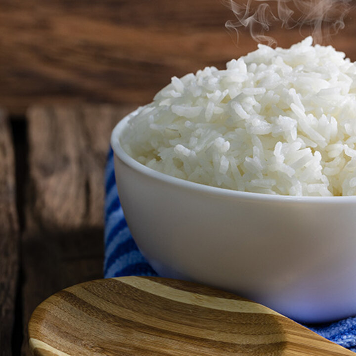 cooked rice in a whole bowl with a wooden spoon and blue towel