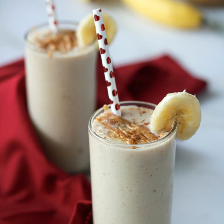 Smoothie in 2 glasses decorated with slice of banana, peanut butter and a straw