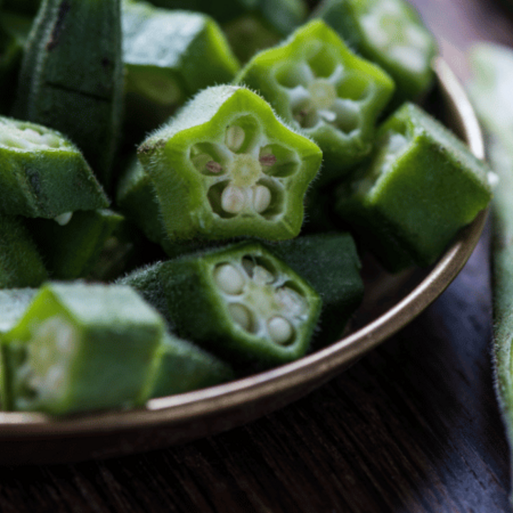 fresh okra sliced in bowl on wooden board