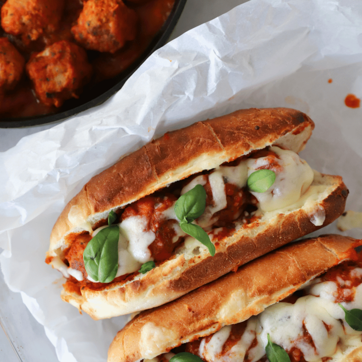 Two meatball subs next to a skillet with meatballs