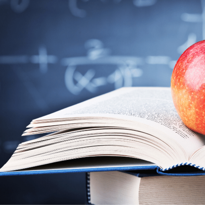 apple on a book in a classroom with a blackboard in the background