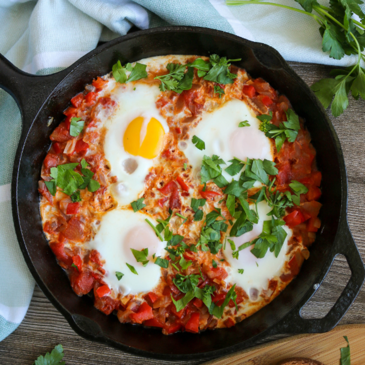 Shakshuka in a skillet with whole wheat bread slices and parsley