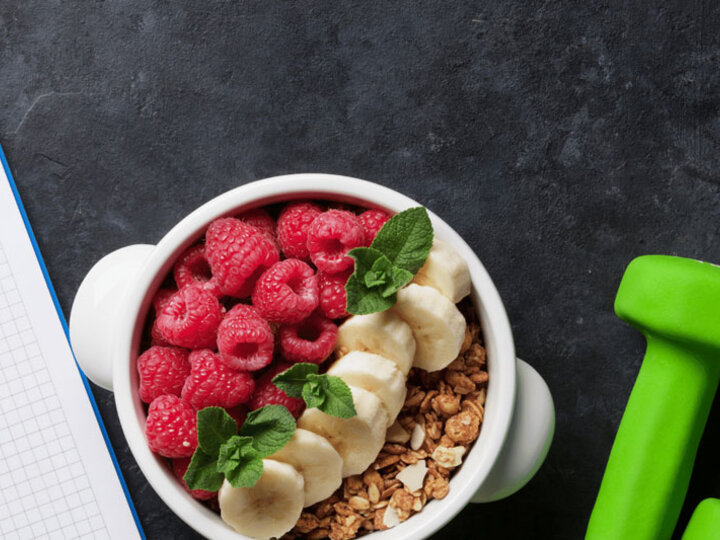 Notebook, bowl of cereal with fruit, and green weights on a table