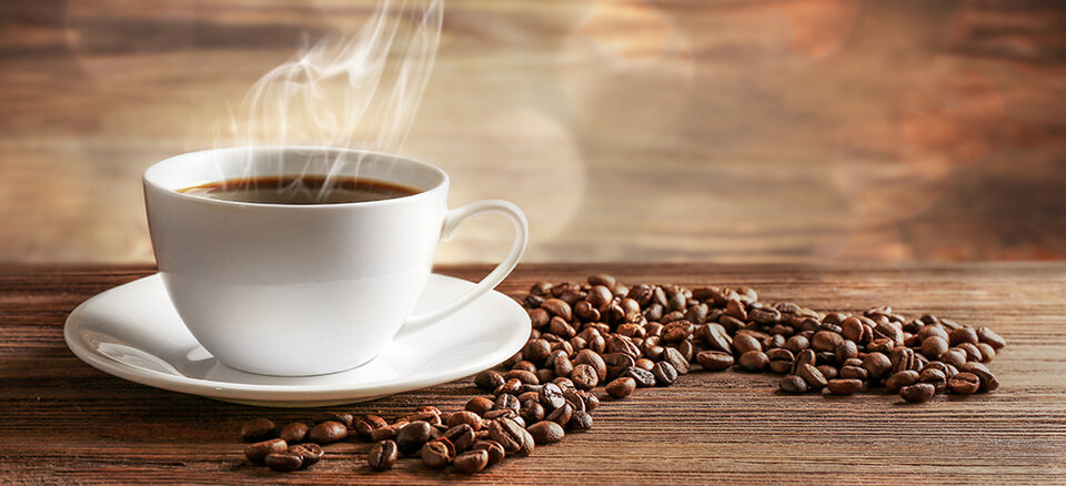 Hot cup of coffee on a saucer surrounded by coffee beans