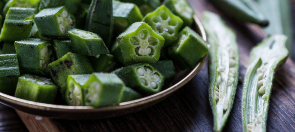 fresh okra sliced in bowl on wooden board
