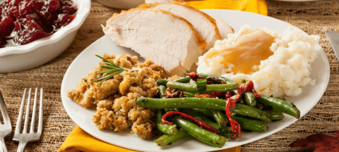 A Thanksgiving dinner plate with turkey, stuffing, mashed potatoes and gravy, and green beans.