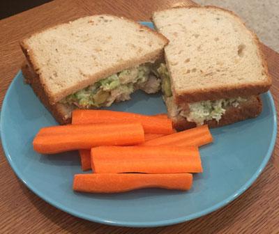 Chicken avocado sandwich on a plate with carrot sticks