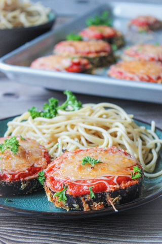 Baked Eggplant parmesan on a plate with whole wheat spaghetti and parsley