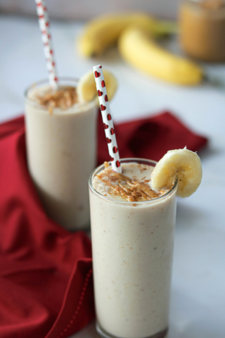 Smoothie in 2 glasses decorated with slice of banana, peanut butter and a straw