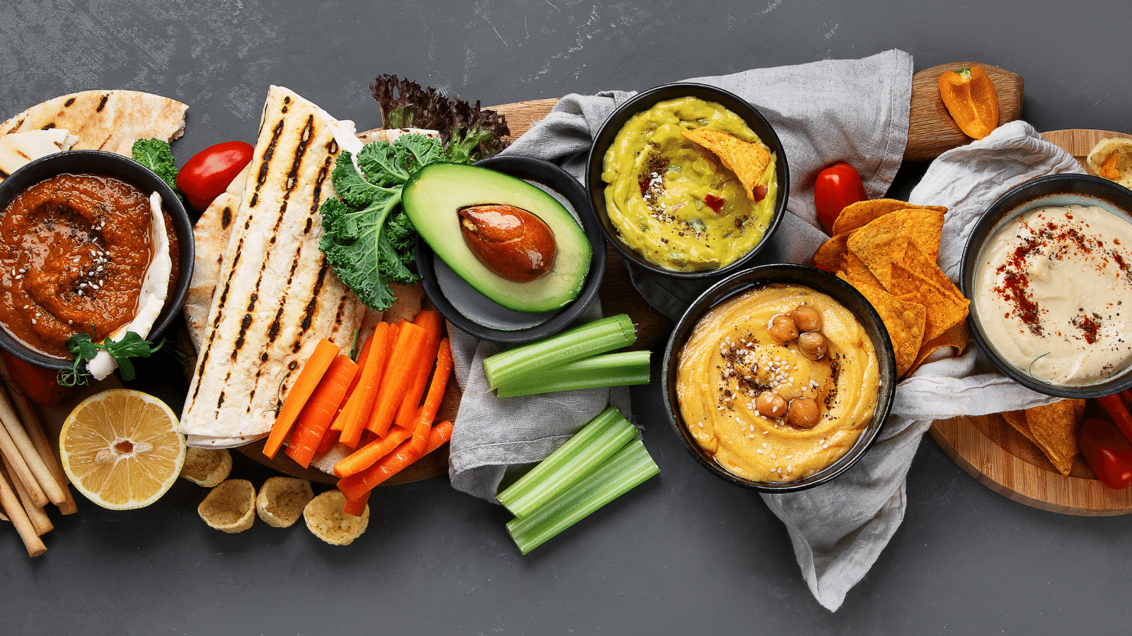 a variety of hummus dips with carrots, celery, and chips